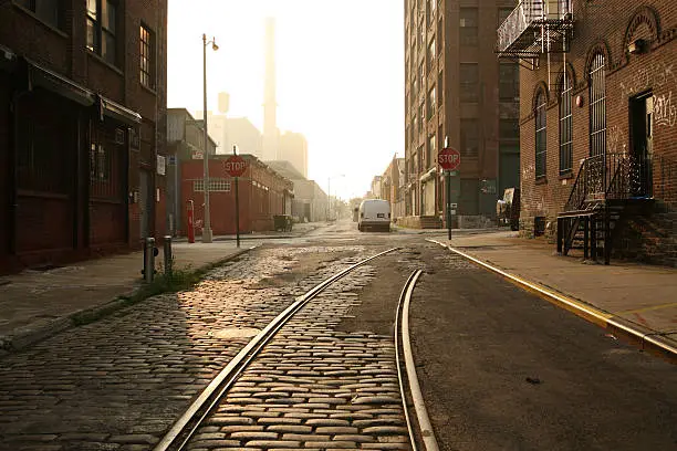"Deserted DUMBO, Brooklyn backstreet at dawn as the sun rises.  Old railway tracks reflect the sunlight."