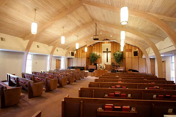 Small church interior with aisle,pews,hymn books, and pulpit with baptistry and cross