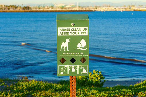 Close-up of a green dispenser with bags for dog waste providing instructions for proper waste disposal.