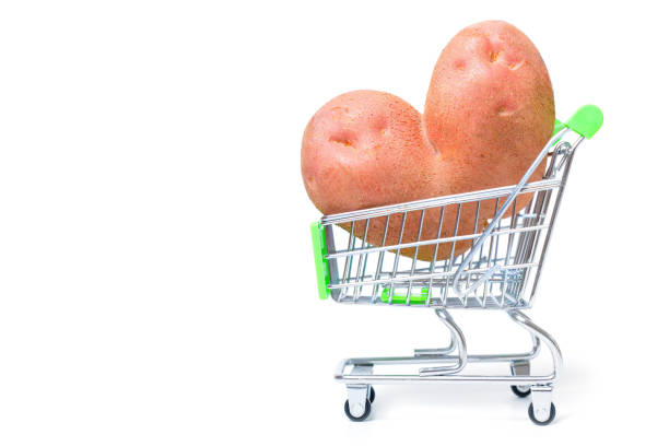 Raw heart-shaped potato in a tiny shopping cart isolated on white background. Online groceries marketplace related concept.