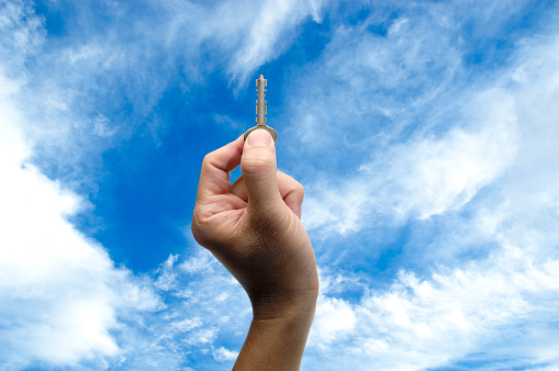 Close up of hand holding a key against blue sky.