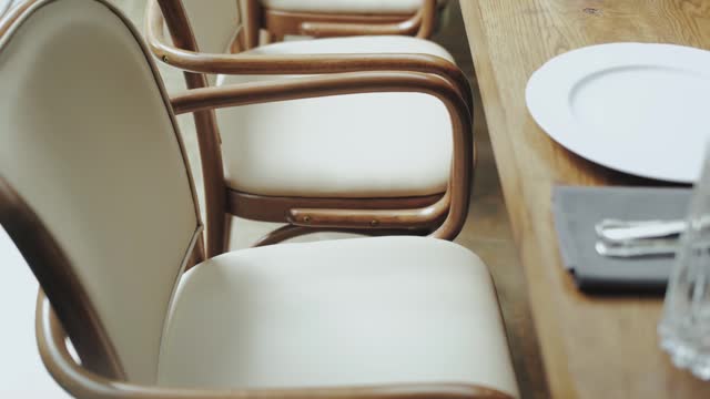Dolly shot close-up cream-colored wooden chairs near the wooden table, indoor wedding celebration. Rustic wedding, slow motion.