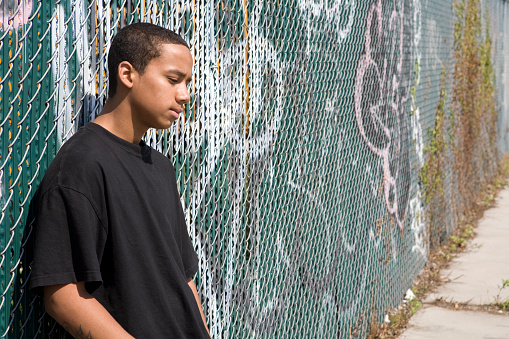 A Puerto Rican teenager standing at a graffiti wall. He looks sad and depressed. Sunny, day in Brooklyn, NY.