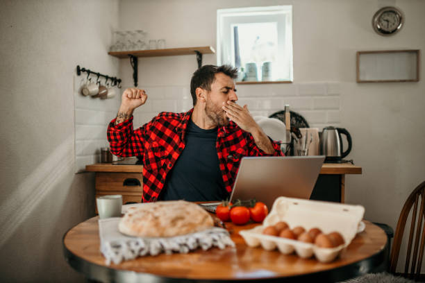 istock A young professional stretches, sips coffee, and works on his laptop at the kitchen table 1723669325