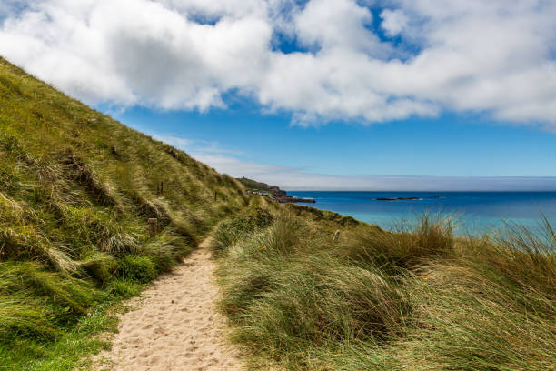 Scenic hiking path on llanddwyn island, anglesey, wales, leading through rocks and grass under a blue sky