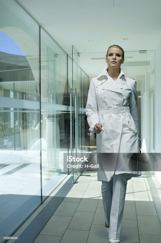 woman in white coat Young blond woman walking inside of a modern office building City Life Stock Photo
