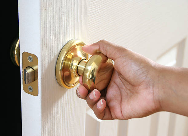 Hand holding a door knob opening a white door stock photo