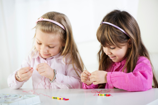 Two Cute little girls making bead Jewelry at home.