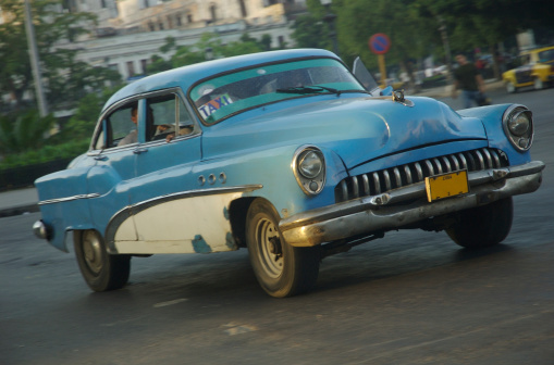 Classic Cuban taxi from the '40s rolls from shadow into the golden light of the rising Havana sun