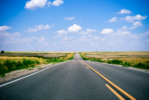 Long two-lane road cutting through the plains. Contains film grain.