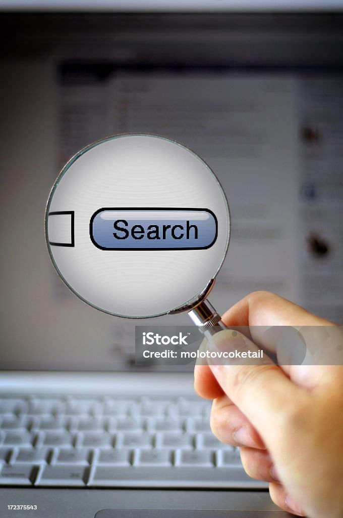 looking for something? Man holding a magnifying glass in front of a laptop. Business Stock Photo