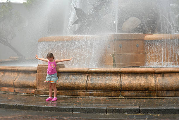 Photography of barefoot girls touching the fountain by legs.  Image with defocued background. Concepts of walking, happiness, childhood and freshness in hot summer day.