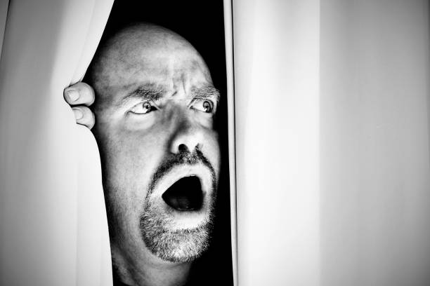 istock Horrified mature man looks sideways through curtains gasping in shock 172376578