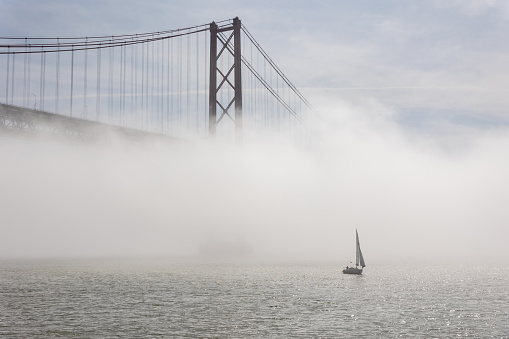 Suspension bridge shrouded in white fog - sailboat sails the sea. Mid shot