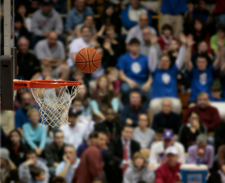 A basketball flies through the air towards the rim with the stands full of out of focus fans in the background.