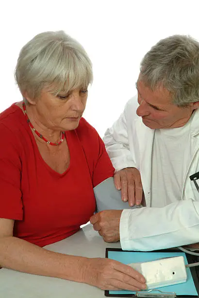 Doctor applying the bloodpressure band at the arm of a senior female patient.