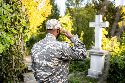 Close up view of soldier standing in front of his friend’s grave and saluting.