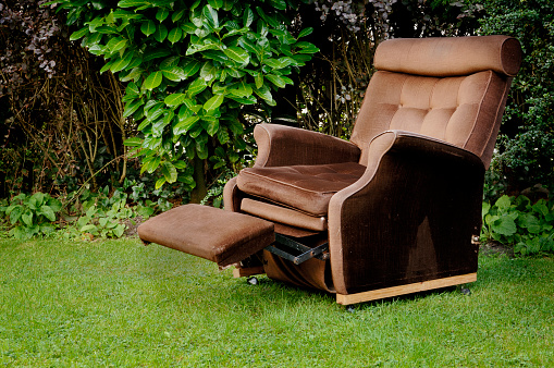 Old worn corduroy reclining chair in a garden.
