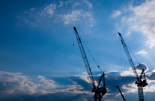 Cranes backlit on a blue cloudscape.