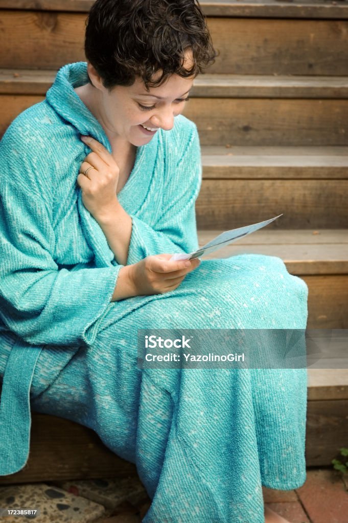 Joyful Letter (series) "Woman with smile, positive emotions, reading a letter/card.  Wearing silver wedding band and bathrobe.  Sitting on porch outdoors. Part of series also includes model unhappy/serious reading letter.See more from this model:" 35-39 Years Stock Photo