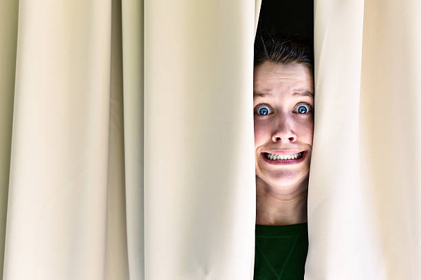 istock Grimacing in terror, young wman looks through curtains 172386291