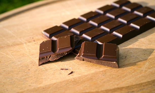 A broken bar of dark chocolate on a wooden cutting board Dark chocolate candy bar on a cutting board. (SEE LIGHTBOXES BELOW for many more desserts, sweet food, baking, & snack photos...) chocolate bar photos stock pictures, royalty-free photos & images