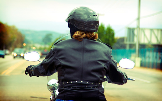 A woman with a leather jacket heads down the road on her motorcycle.