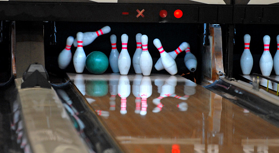 Bowling ball smacks a set of pins at a bowling alley.