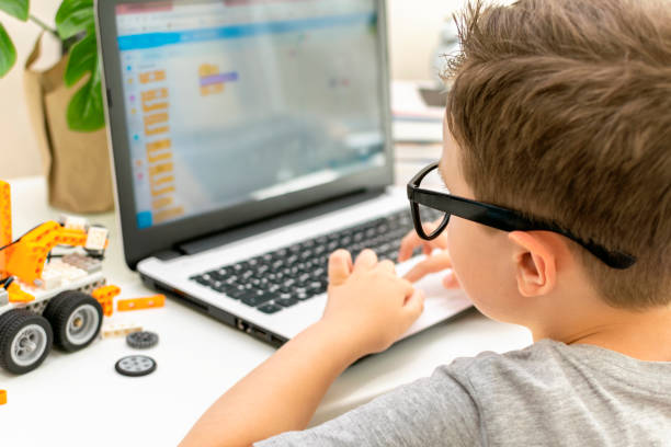 istock Little boy student in glasses builds and programs a robotic vehicle codes an electronic toy. Child using laptop in science class. Rear view. 1723868002