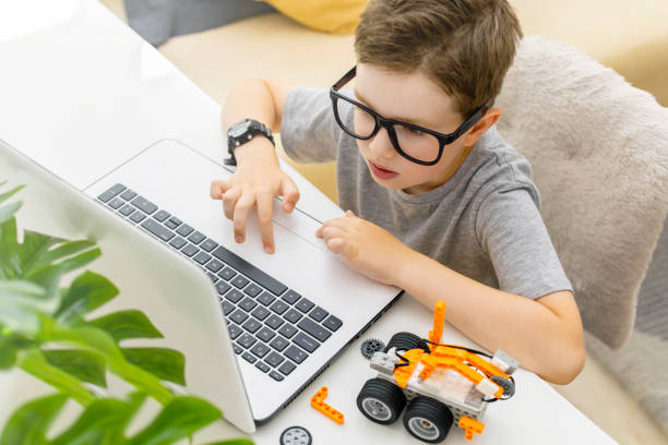 istock Clever young schoolboy in glasses builds and programs a robotic vehicle codes an electronic toy at home. Child using laptop. 1723868014