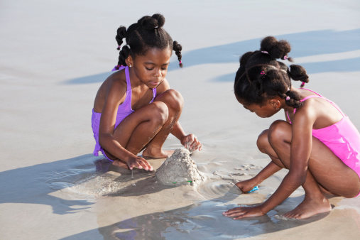 African American girls (twins, 6 years) playing with sand at the beach.