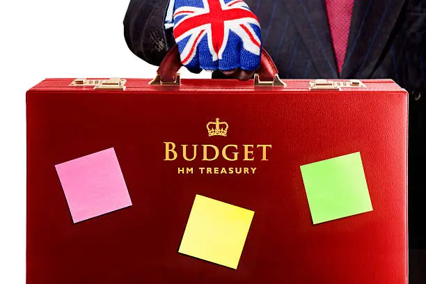 "The Chancellor of the Exchequer presents the UK fiscal Budget, contained within the traditional red briefcase. Post it Notes are for highlighting key changes in the Budget announcement, such as, Pink for increases in taxation, etc, Green for reductions in taxation or general tax benefits and Yellow for neutral announcements. Good copy space. Isolated on white. The United Kingdom Budget statement is made by the Chancellor of the Exchequer, a member of the Government  who is responsible for all economic and financial matters. He controls and is responsible for HM Treasury and the revenues gathered by Her Majesty's Revenue and Customs and the expenditure of public sector departments. He raises and lowers taxes and duties according to the needs of the economy. After the Prime Minister he is the most important state officer. The Budget is normally an annual event in March, but in more recent times a mini budget has also been held in November. The budget speech is always carried to the House of Commons in a red briefcase, known as Ministerial Boxes, or Red Boxesaa. This red briefcase has become representative of the annual UK Budget. Historically, it dates back to the first use by William Gladstone in 1860."