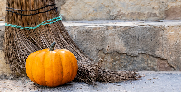 Beautiful orange fresh pumpkin in front of old broom on stone background with space for poster, greeting invitation, business banner. Halloween design concept. Outdoor photography, natural daylight.