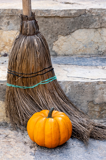 Beautiful orange fresh pumpkin in front of old broom on stone background with space for poster, greeting invitation, business banner. Halloween design concept. Outdoor photography, natural daylight.