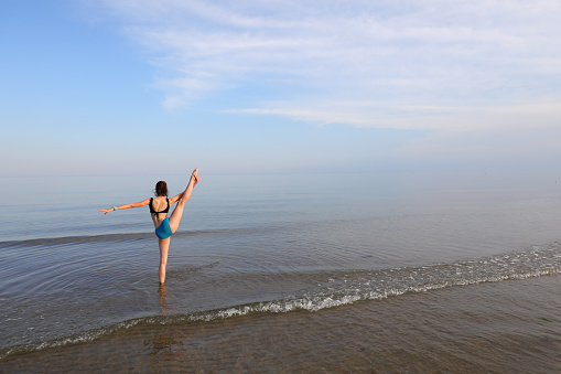 athletic girl with leg up during seaside toilet exercise on the beach