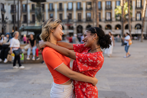 Side view photo of cure multi-ethnic lesbian tourist embracing looking each other in the city