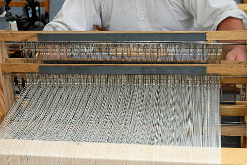 ancient wooden loom for weaving fabrics with many white threads that must be carefully worked by the Weaver