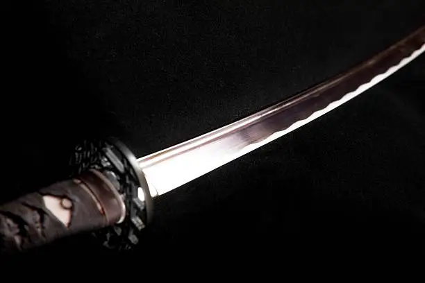 A selectively lit samurai sword on a black background