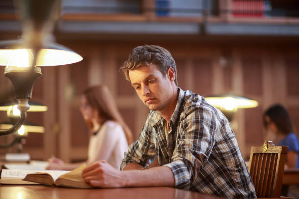 Young man reading in library at night stock photo