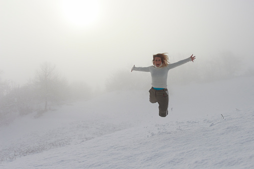 Mid-adult woman jumpin in snow. Flying with hands outstretched. Towards camera.