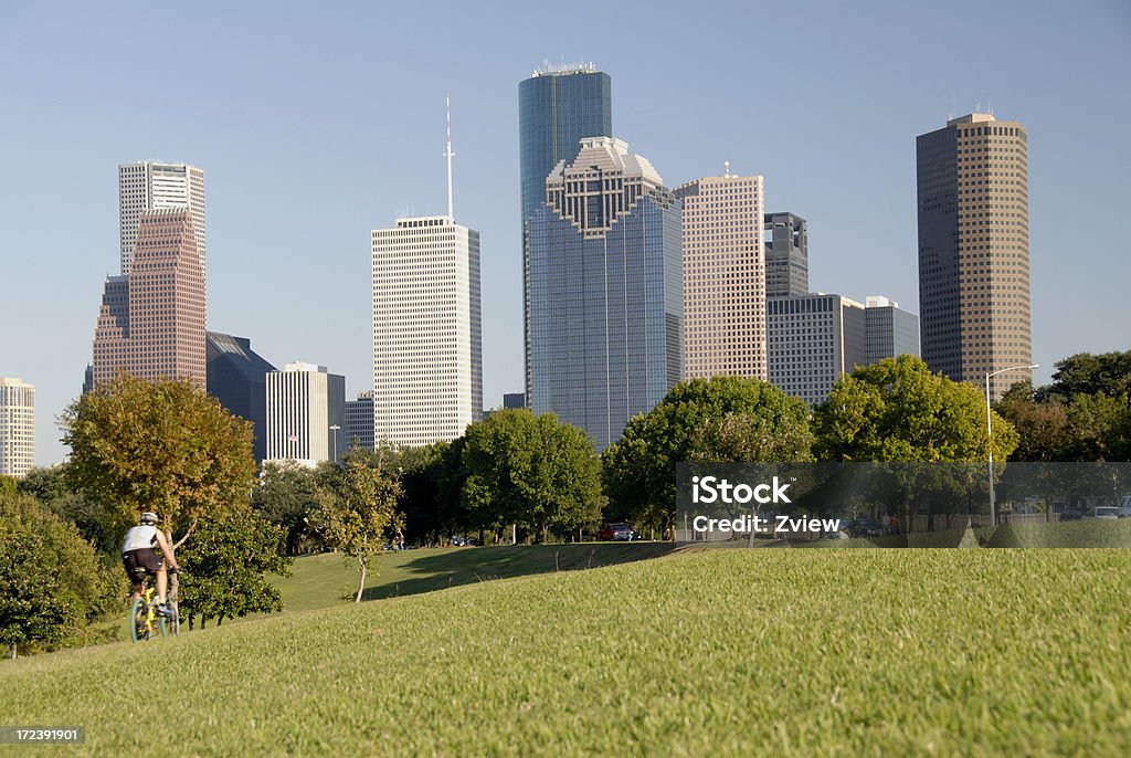 Bicycling Through A City Park -  Skyline In Background "a bicyclist takes advantage of a beautiful fall day has he zooms through a city park in Houston, Texas. Modern city skyscrapers and the beautiful clear blue sky can be seen in the background.  The bicyclist has slight motion blur." Houston - Texas Stock Photo
