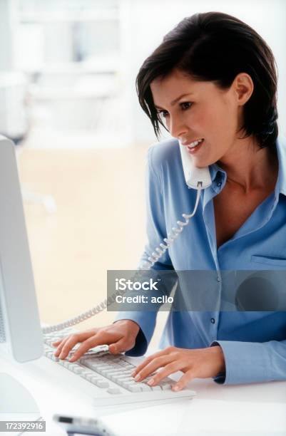 Mujer Haciendo Una Llamada Mientras Escribiendo En Su Teclado Foto de stock y más banco de imágenes de Varios oficios