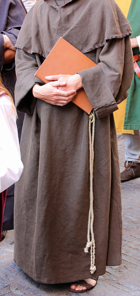 Franciscan friar with the brown dress called habit and the rope around his waist with the sacred book on hand and sandals on feet
