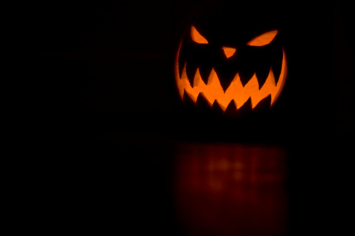 A candle lit and carved pumpkin casting a relection on a wooden floor.