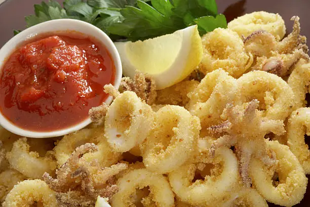 Close up of Fried calamari with marinara sauce and lemon.