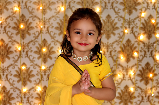 Small baby girl celebrating Diwali festival at home against light background. Diwali is the Hindu festival of lights with its variations also celebrated in other Indian religions. It symbolises the spiritual \