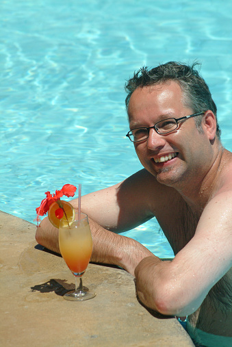 Young man with cocktail in Kenyan swimming pool.