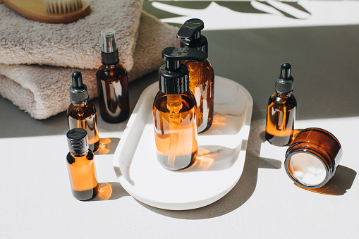 Amber bottles with facial treatment on a white tray with green leaves on backdrop. Top view