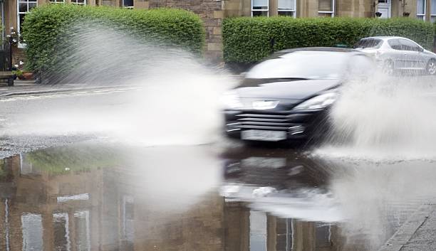 A car splashes through a large puddle on a wet road.