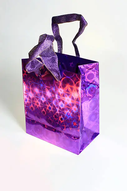 Bright Purple Festive Hollographic Shopping Gift Bag shot and isolated on a white background and this present bag comes with a clipping path. It's bright, reflective and shiny, that makes cool patterns with the light. I perfect image for shopping carts and mail order catalogs.